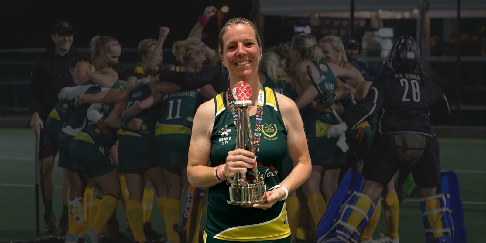 Lauren Penny in South Africa kit holding the Masters World Cup trophy, with her celebrating team behind her